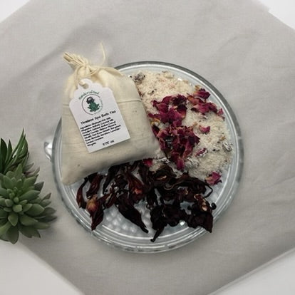 A jar labeled 'Stirrers in the Ancient Art of Bath Tea Rituals' with a black lid, alongside a beige tea bag and a tag with the product information.