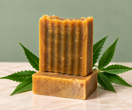 Neem Renewal handmade cleansing bars stacked against a muted sage background, surrounded by green neem leaves, showcasing their natural golden-brown color and textured finish.