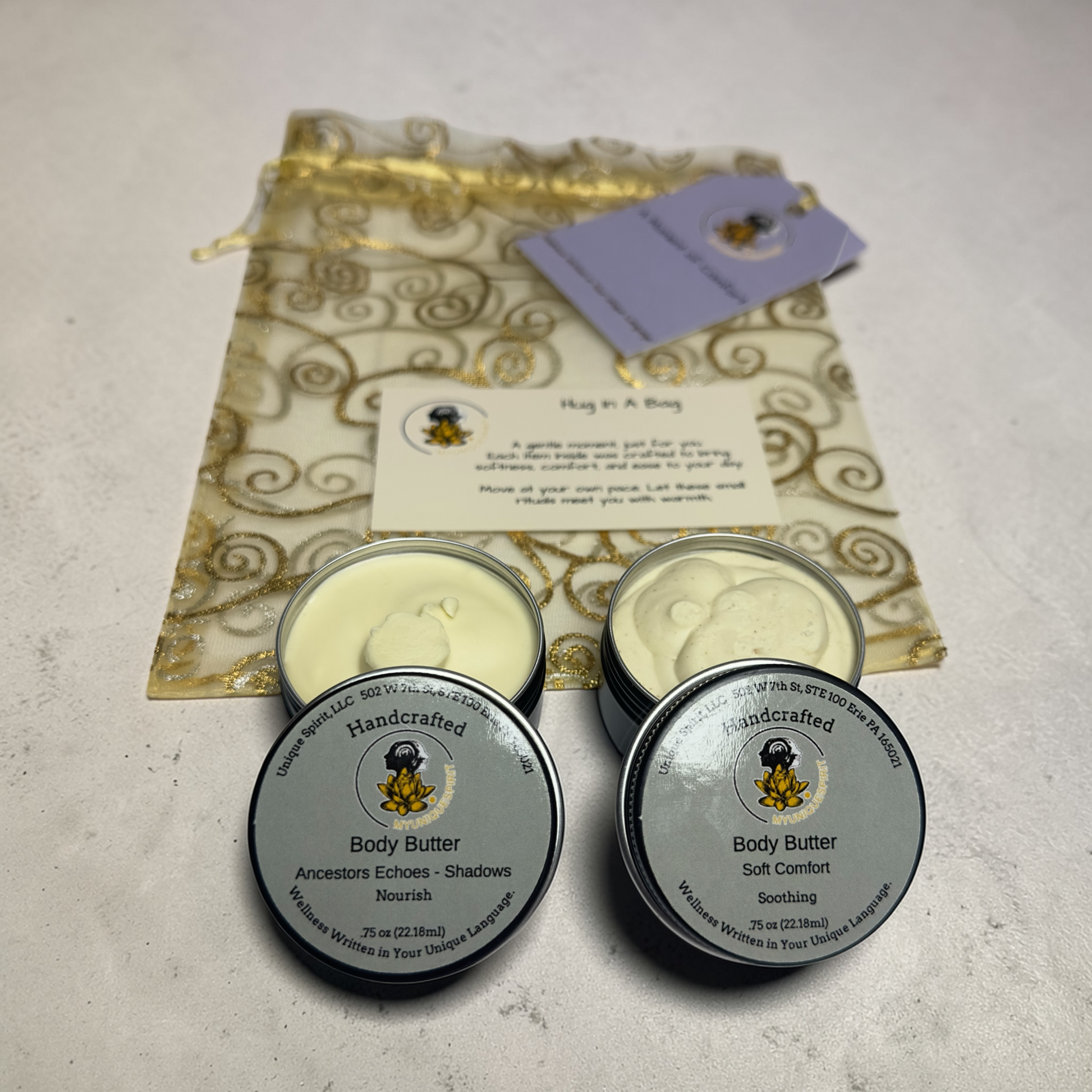 Three tins of handcrafted body butter with a decorative bag and card on a light background