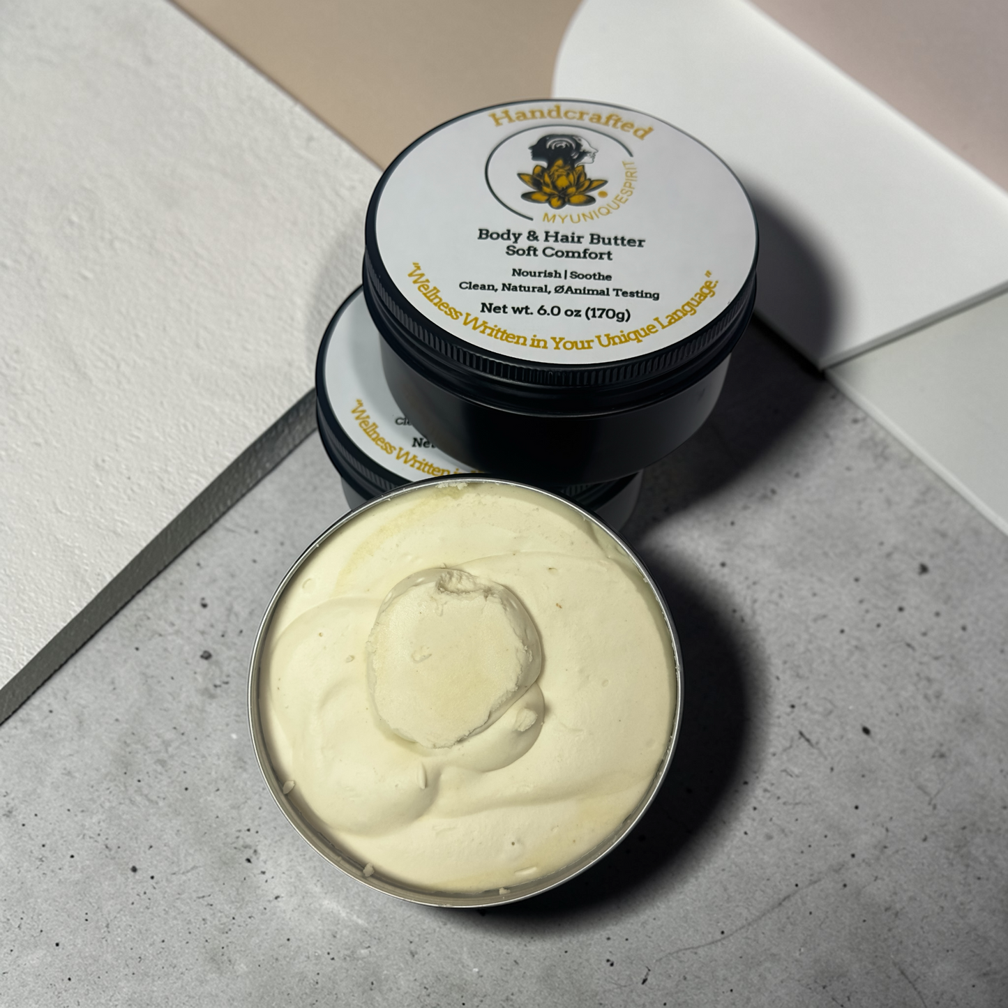 Two containers of body and hair butter on a concrete surface