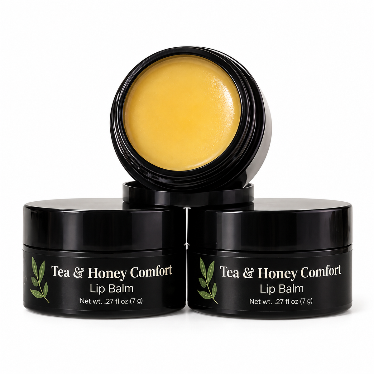 MyUniqueSpirit Tea & Honey Comfort Lip Balm in black jars, one open to reveal golden balm, displayed with chamomile flowers, herbal tea, honey, and honeycomb on a marble surface.